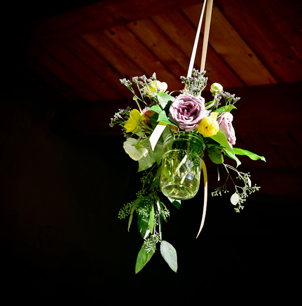 image of purple, yellow, and green floral arrangement in a fruit jar hanging by a tan ribbon from the ceiling - photo by New Mexico based wedding photographers Twin Lens